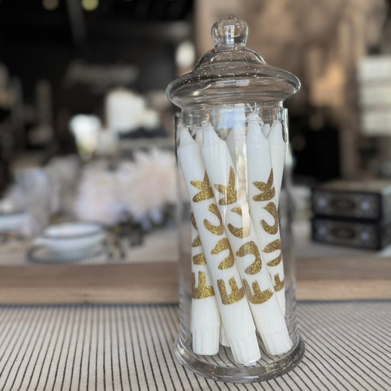 Glass jar with white candles featuring gold deer designs on a blurred background