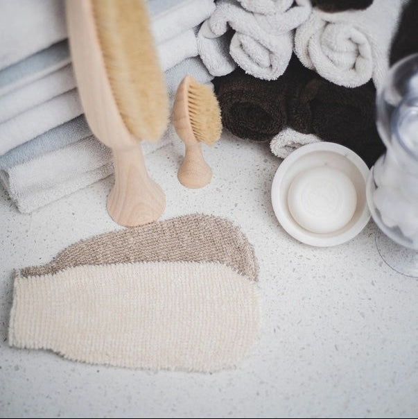 Bath brushes and loofah on a towel with a neutral background