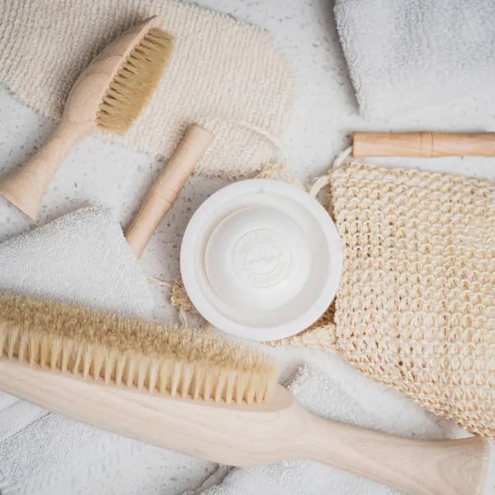 Set of natural cleaning tools including brushes and a soap dish on a textured surface.