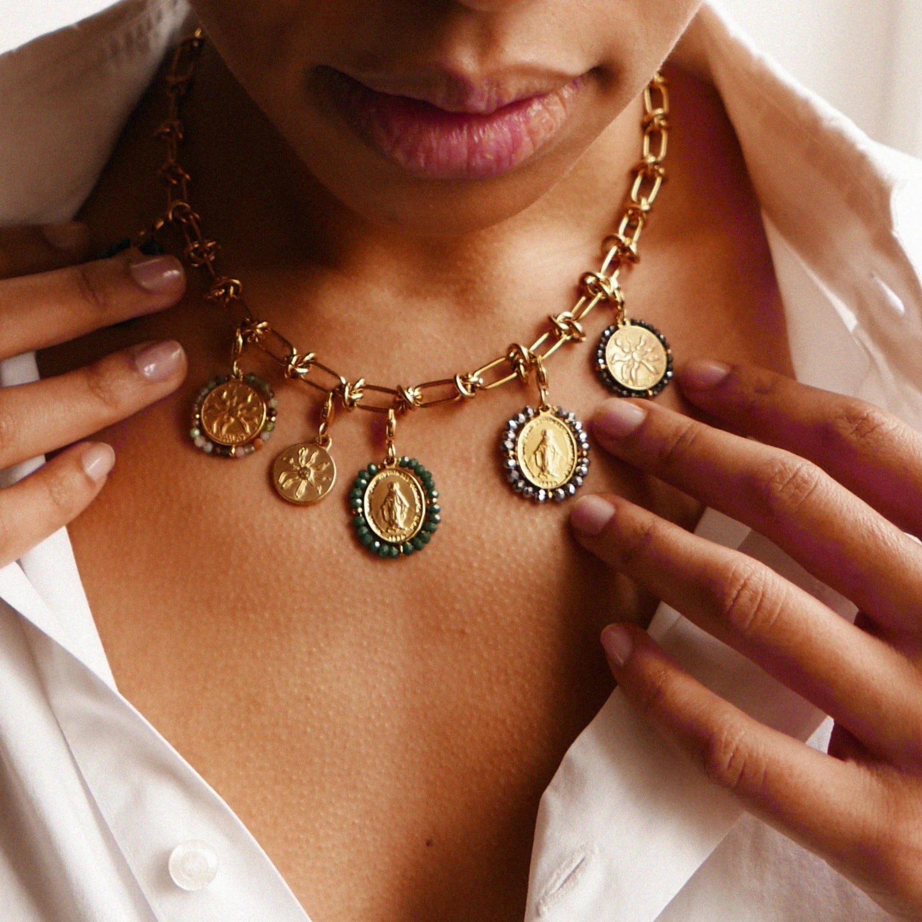 Close-up of a person wearing a gold necklace with charms, against a neutral background.