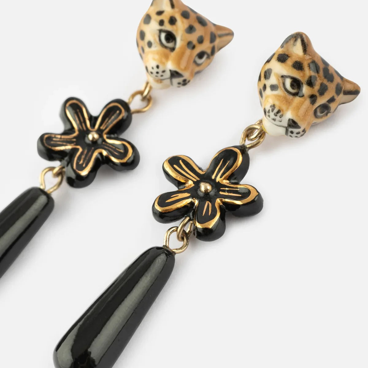 A pair of drop earrings featuring leopard head studs in tan and black, connected by gold chains to black flower charms and glossy black teardrop beads, shown on a light gray background.