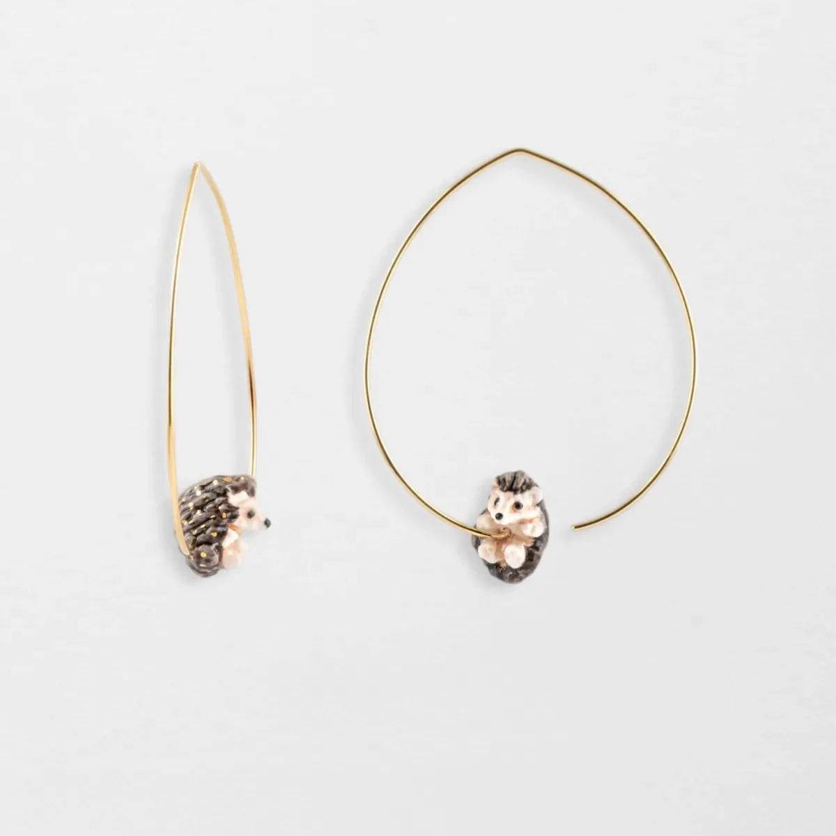 Pair of gold hoop earrings with hedgehog charms on a light gray background