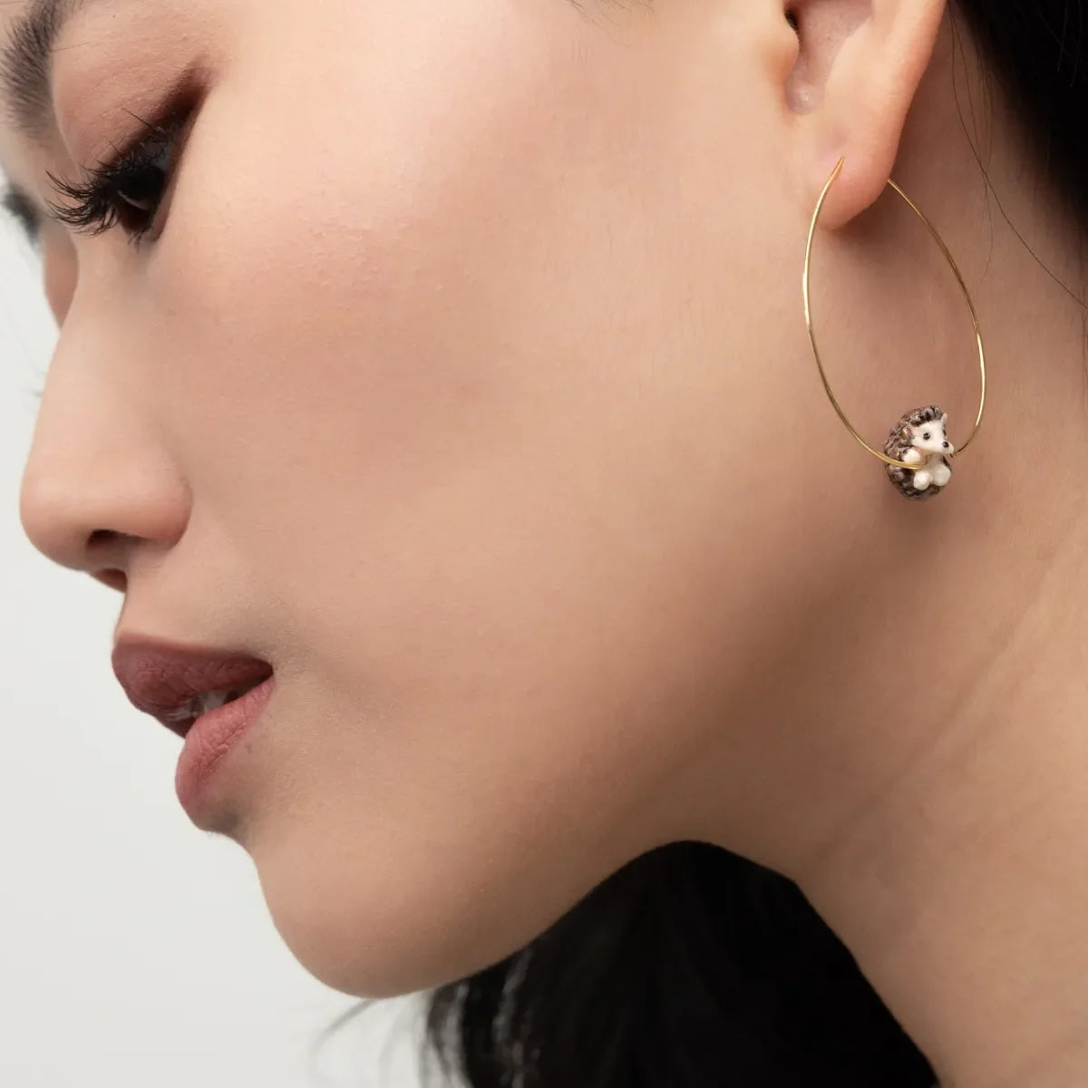 Close-up of a woman wearing gold hoop earrings with a small animal charm.