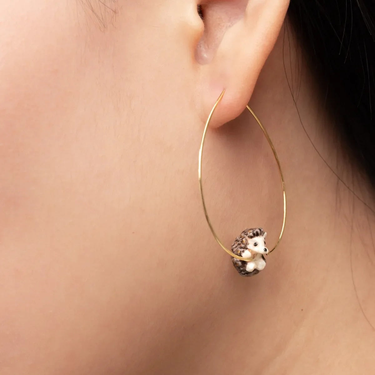 Gold hoop earring with a hedgehog charm worn by a person