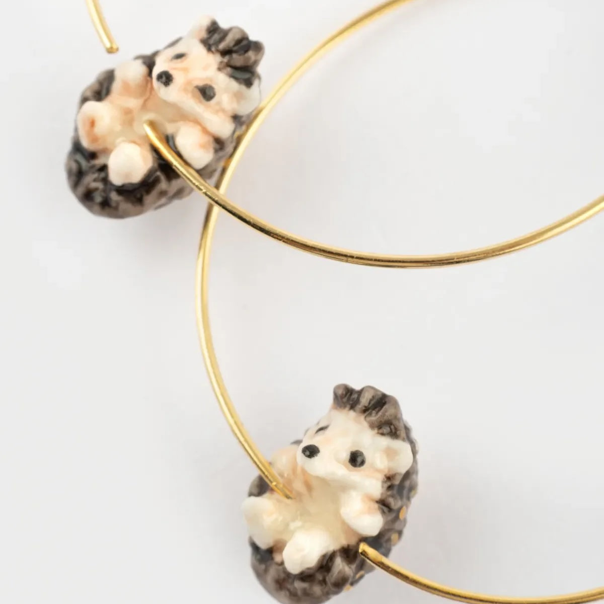 Hedgehog-shaped earrings on gold hoop earrings against a white background