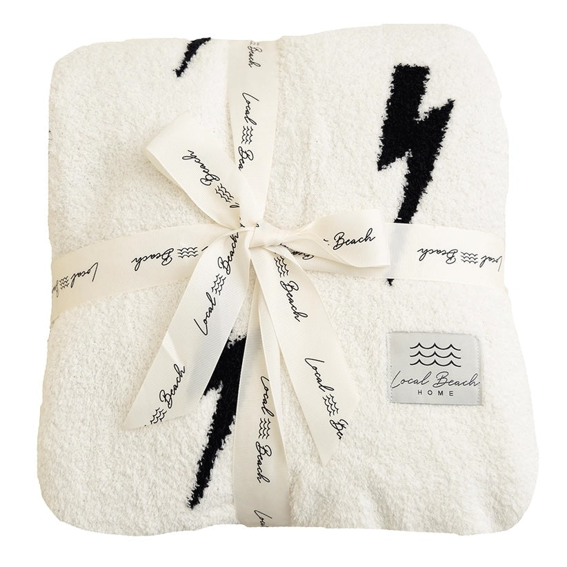 White blanket with black lightning bolt designs and a bow, branded 'Local Beach Home'.