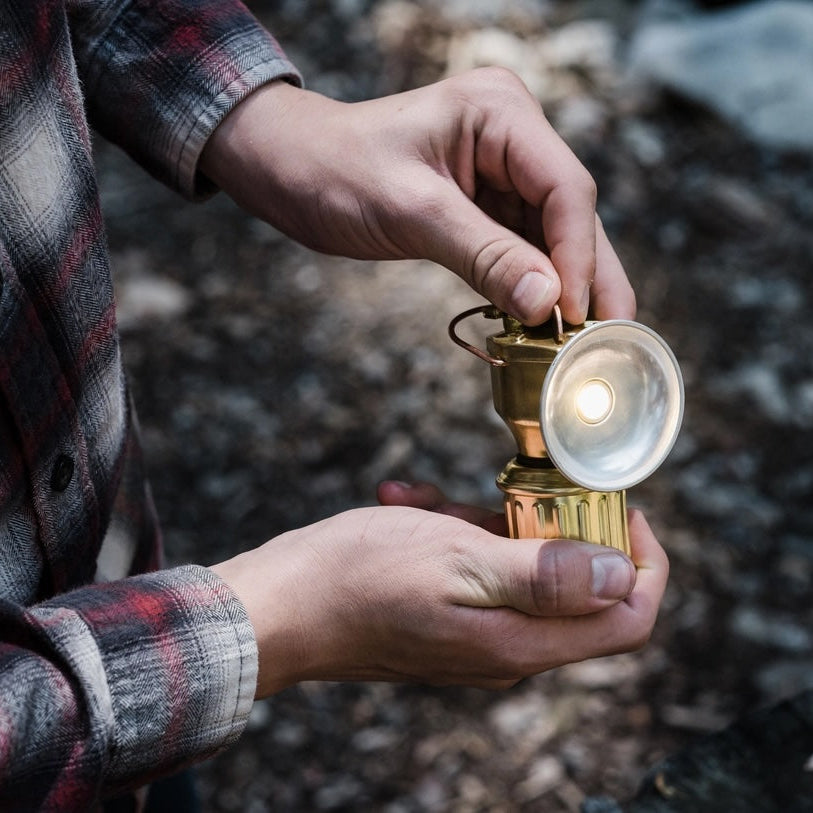 Person holding a vintage-style lantern outdoors on a rocky ground