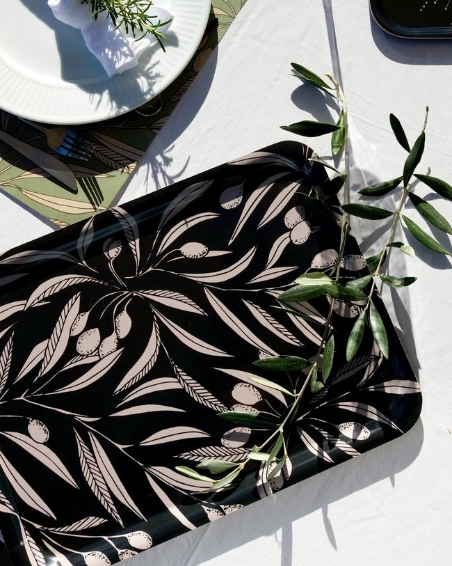 Black tray with white leaf pattern on a white tablecloth with green leaves.