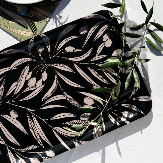 Black tray with white leaf pattern on a white tablecloth with green leaves.
