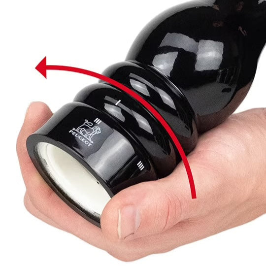 Black pepper grinder held in a hand with a white background