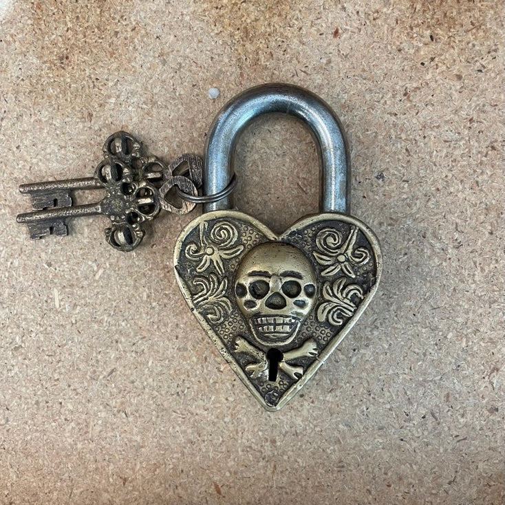 Heart-shaped lock with skull design and key on a textured surface