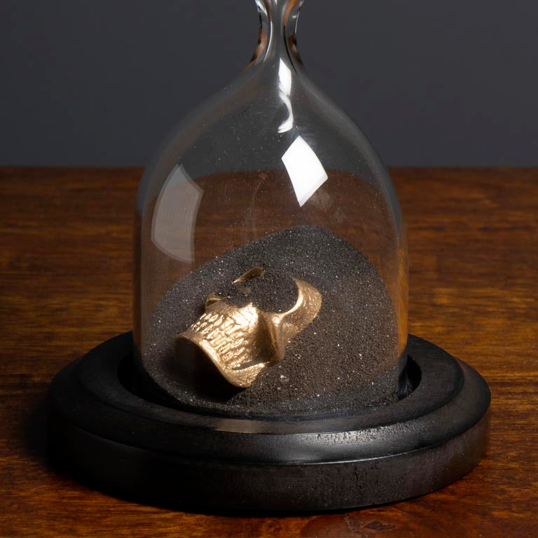 Gold skull figurine inside a sand timer on a wooden surface