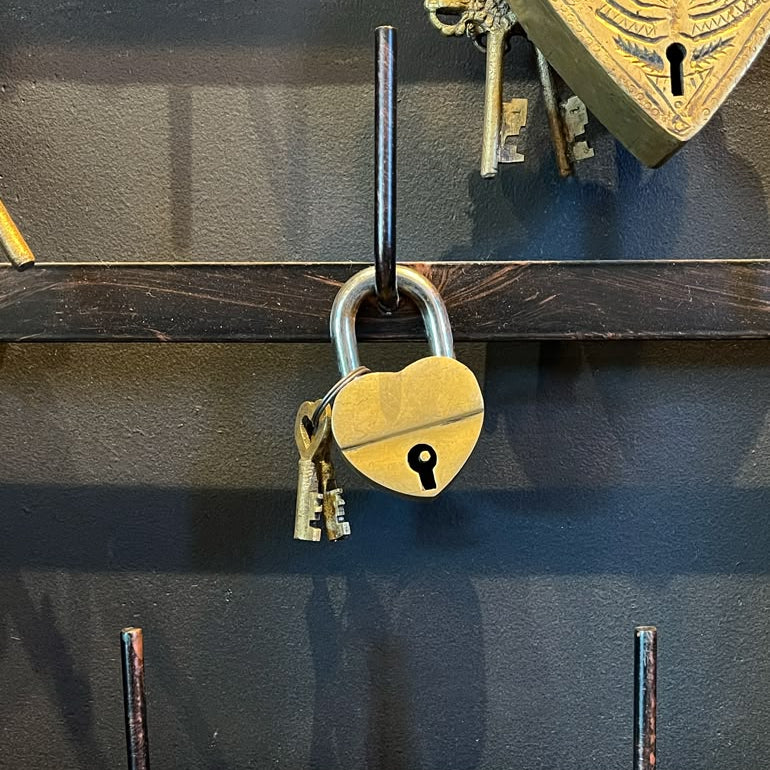A gold-colored, heart-shaped padlock with two keys hanging on a dark wooden surface.