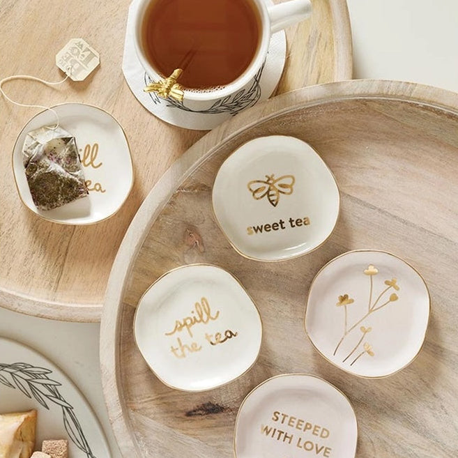Set of small ceramic dishes with tea-themed designs on a wooden tray with a cup of tea.
