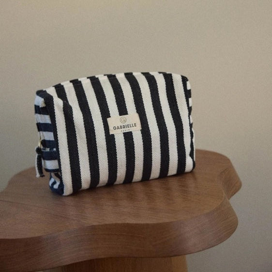 Black and white striped pouch with a brand label on a wooden surface against a beige wall.