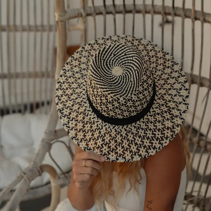 Person wearing a black and white patterned sun hat on a wicker chair.