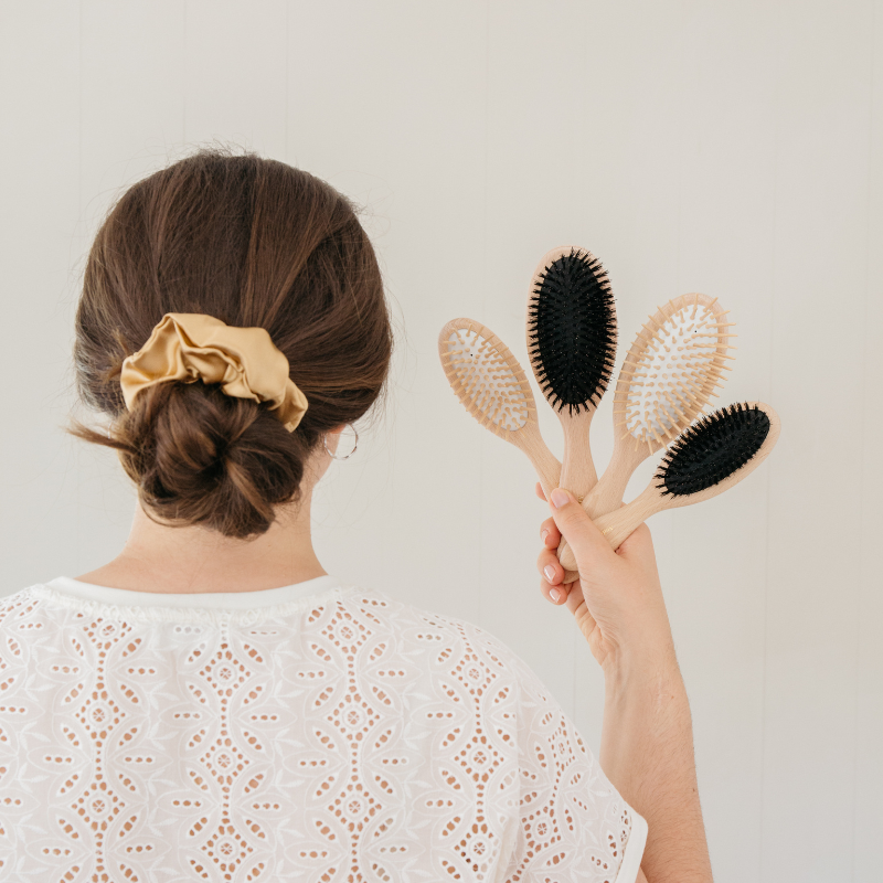 Hand holding both sizes of the beech hair brush behind a braided low bun – Andrée Jardin