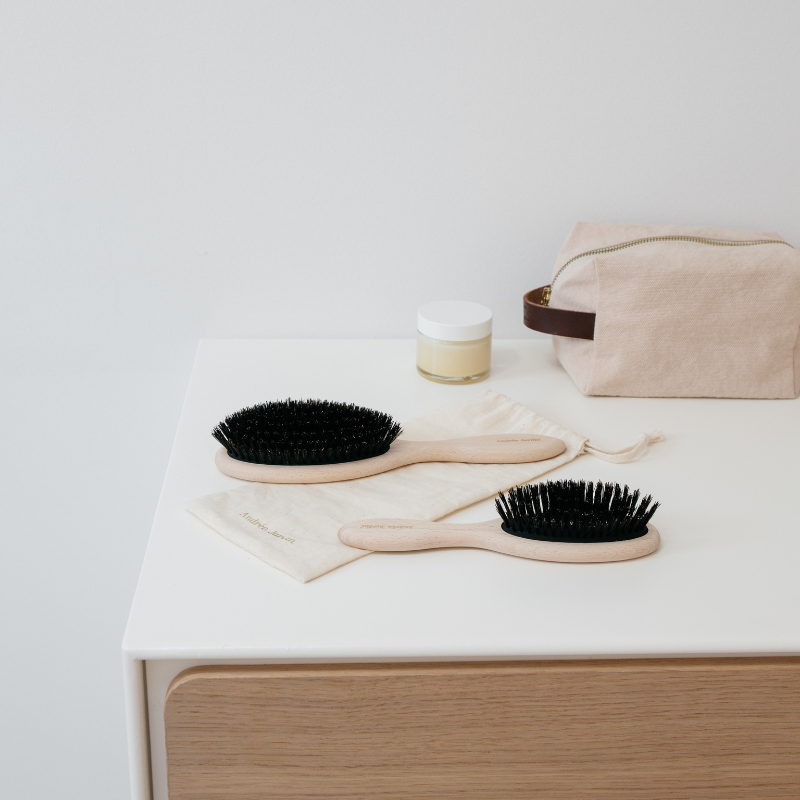 Large and small boar bristle brushes side by side on a white console with a soft pink pouch – Andrée Jardin