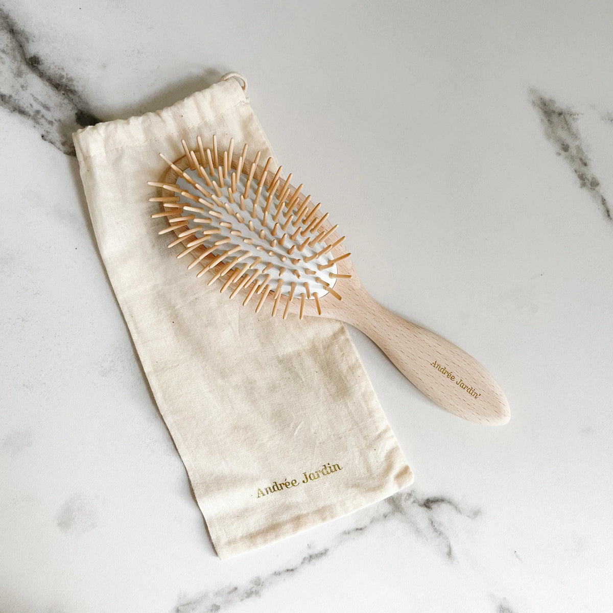 Pale beech brush with fine wooden pins lying on its cream cotton pouch on marble – Andrée Jardin