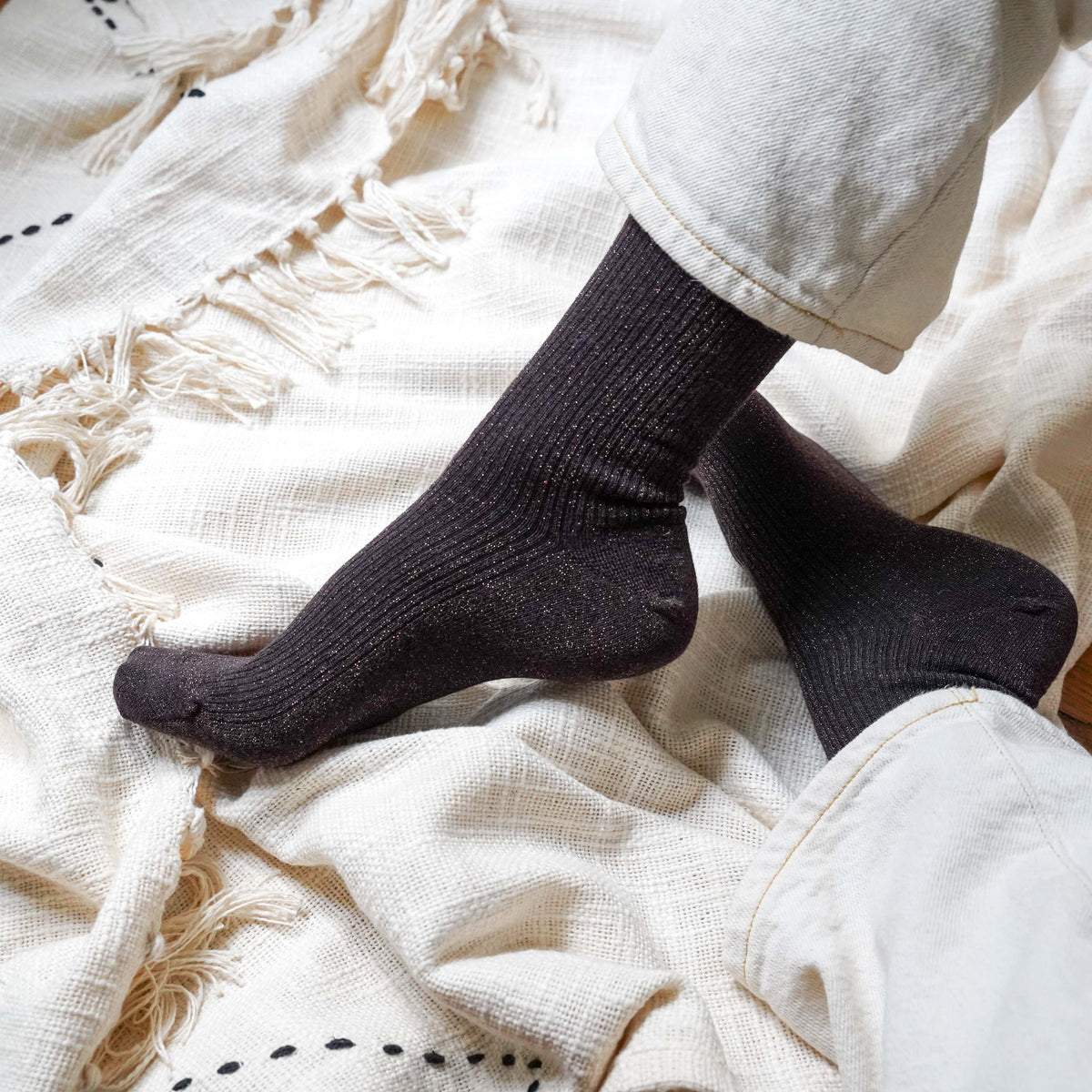 Dark chocolate glitter socks on crossed feet over a cream throw – KLUE
