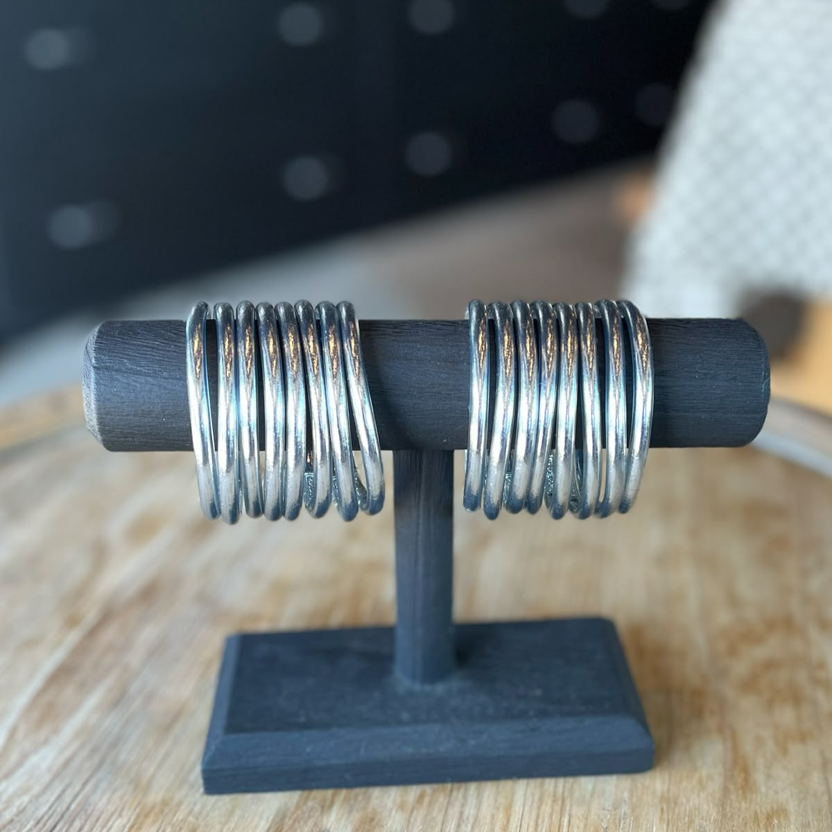 A silver bracelet displayed on a dark wooden stand, with a textured surface and designed with gold leaves.