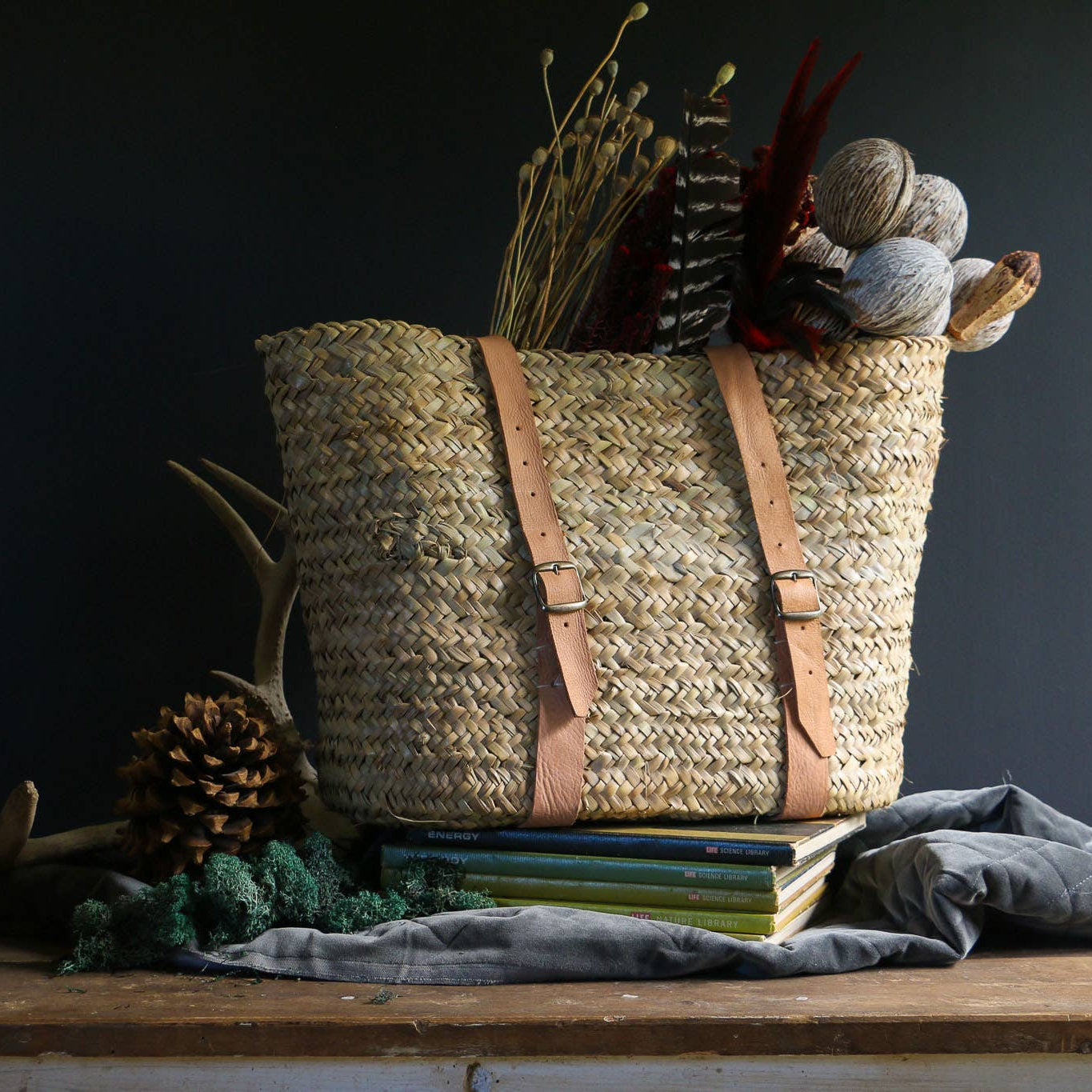 Woven palm basket with two tan leather straps and metal buckles, styled with dried flowers – Medina