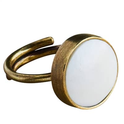 A gold-toned metal open-band ring featuring a large, round, white inlay or stone on the front, set against a plain white background.