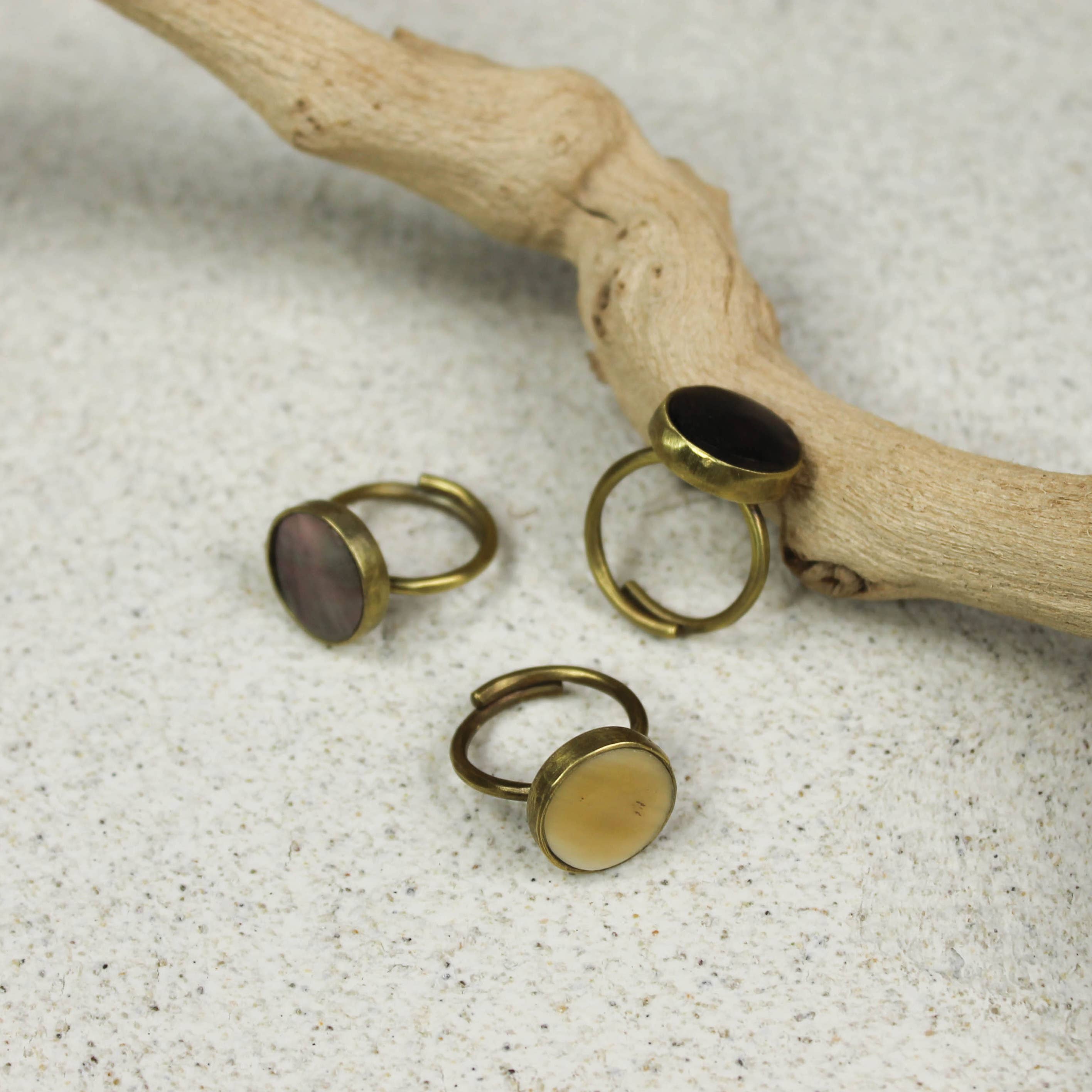 Three rings with different colored stones on a textured surface with a branch.
