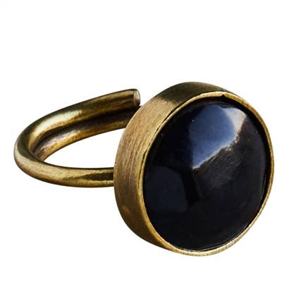 An adjustable open-band ring featuring a large, round bezel-set dark black stone with a brushed antique gold metal setting, shown against a plain white background.