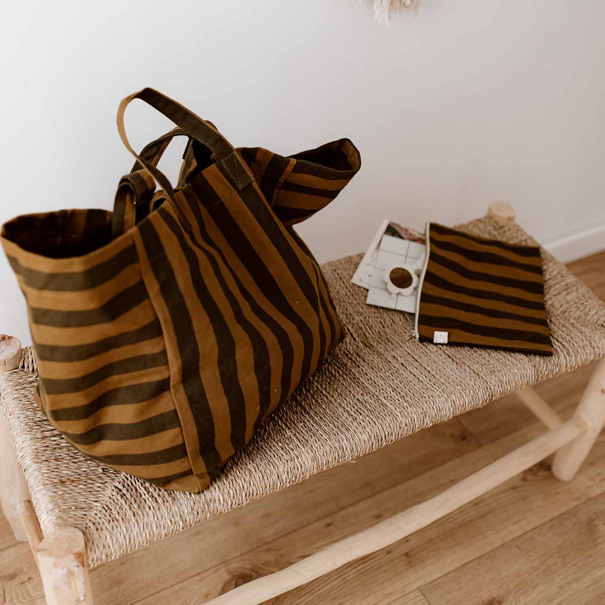 Two striped cumin totes and a matching zip pouch resting on a woven bench – Rose in April