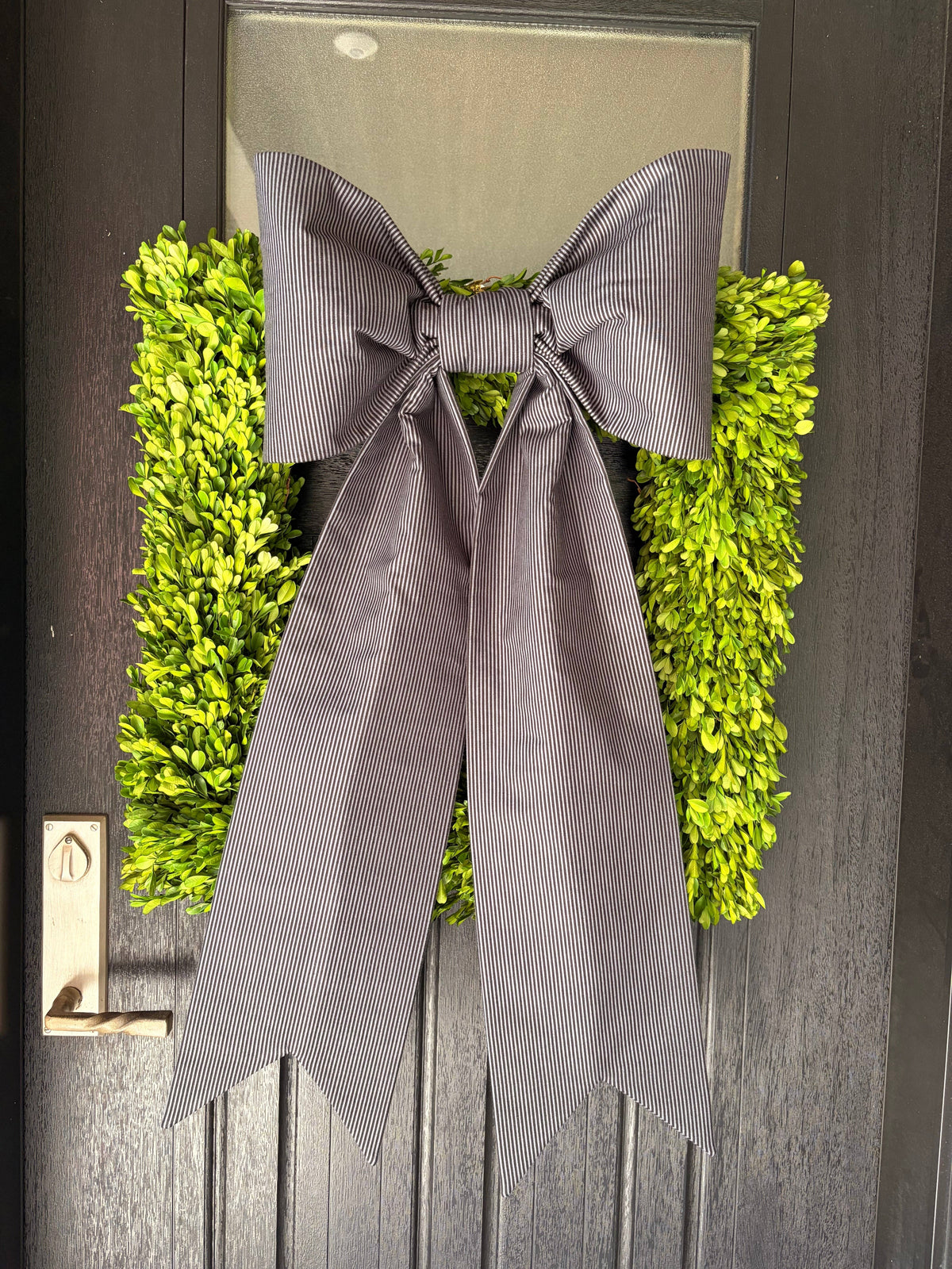Black and ivory ticking-stripe bow over a boxwood wreath on a dark front door – La Maison Reverie