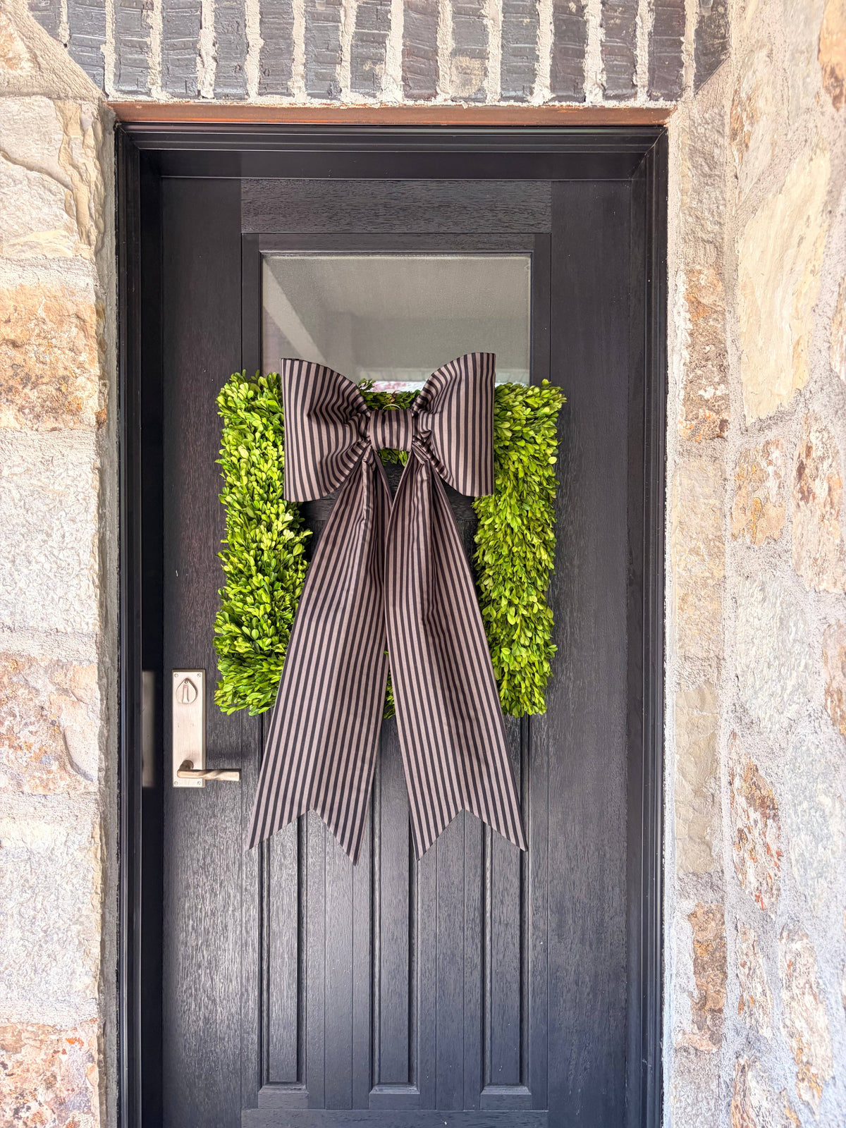 Stone entryway with a charcoal striped bow and green wreath on a black door – La Maison Reverie