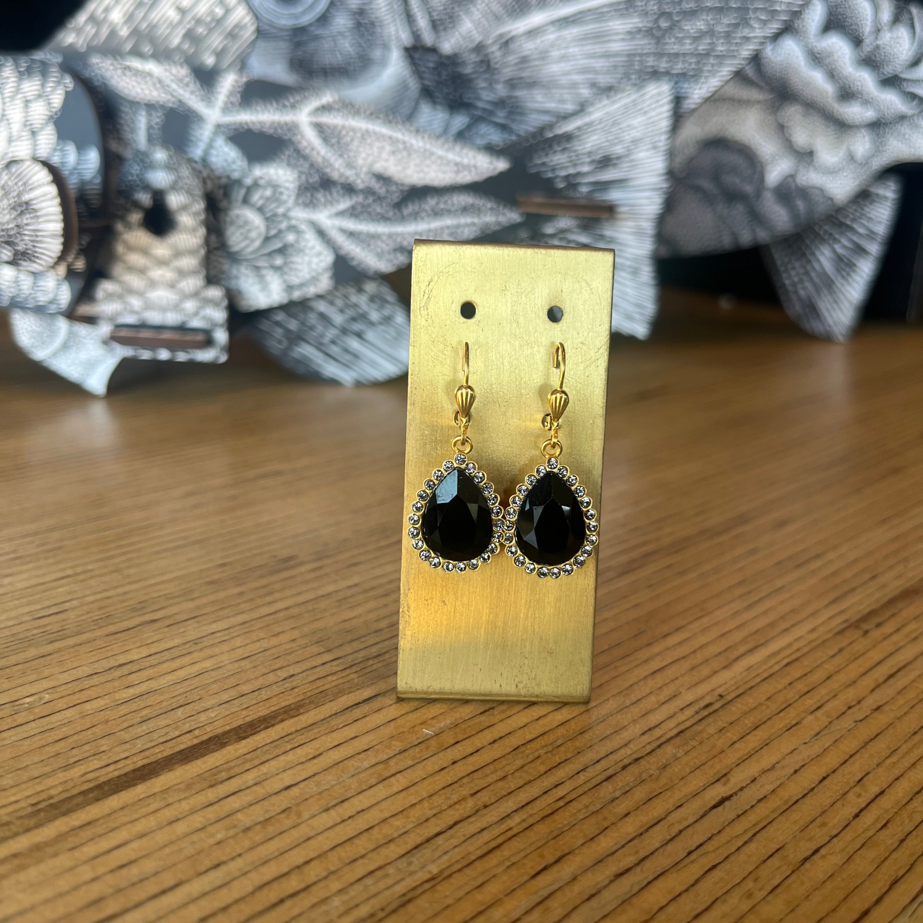 Black earrings on a gold earring stand with a patterned fabric background