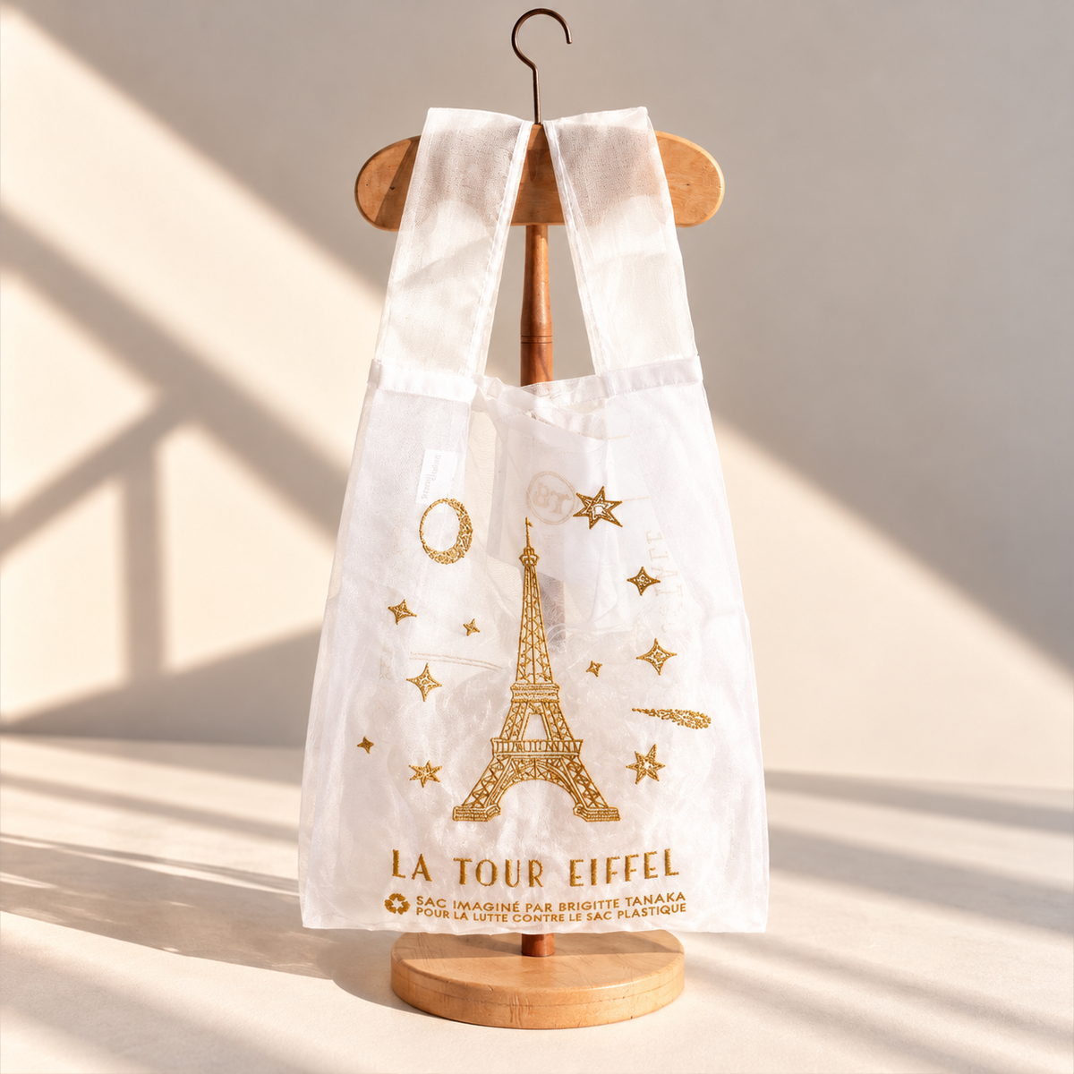 White organza bag embroidered in gold with the Eiffel Tower, moon and stars, on a wooden hanger – Brigitte Tanaka