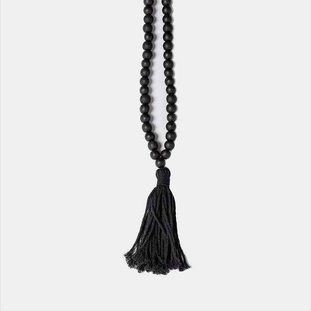 A black beaded necklace with a long black tassel, displayed vertically against a light gray background.
