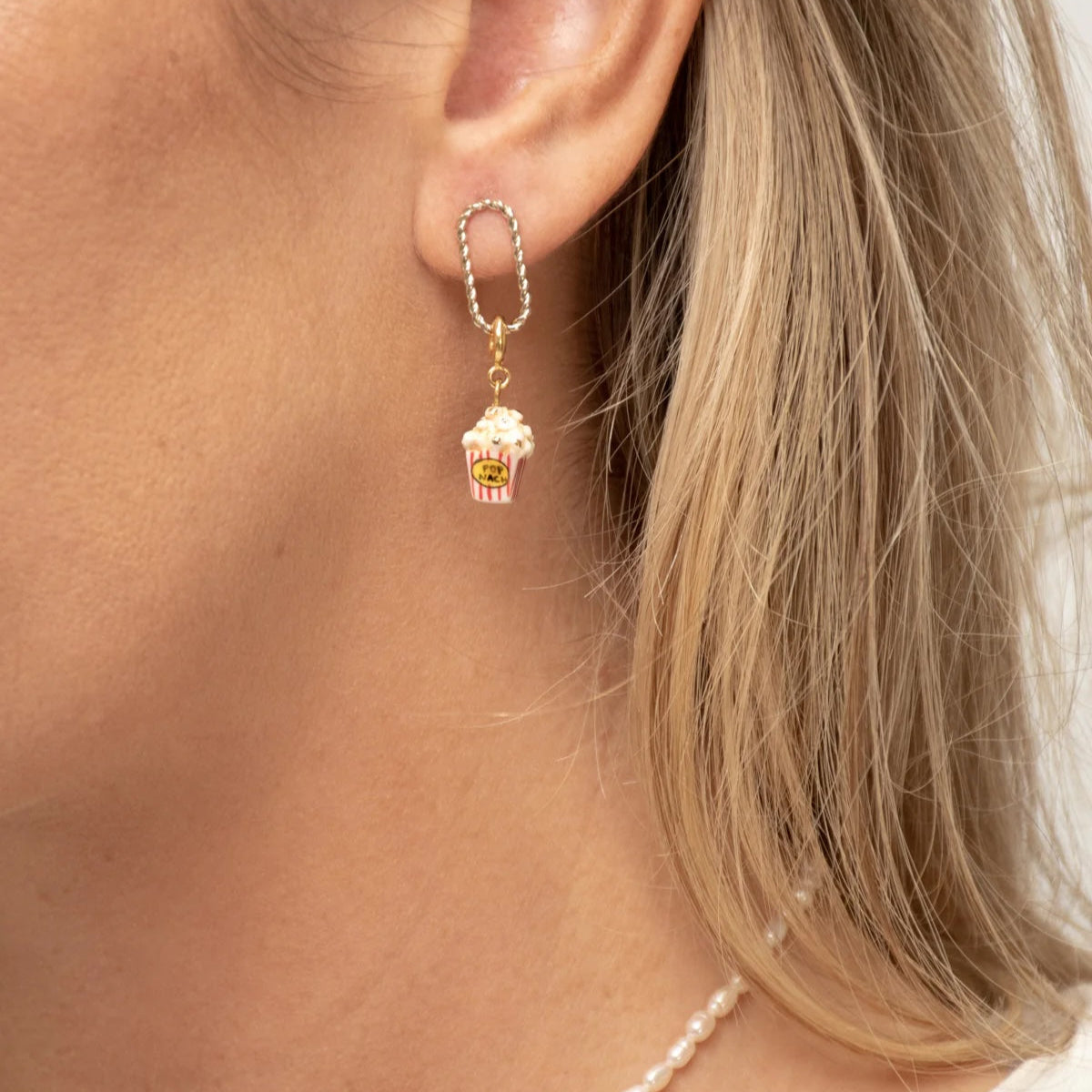 Close-up of an earring with a small cupcake charm worn by a person with blonde hair.