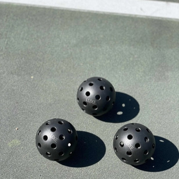 Three black pickleballs  on a green surface