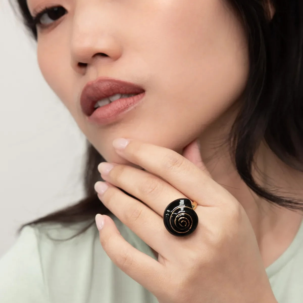 Woman wearing a black ring with a snail design on a plain background