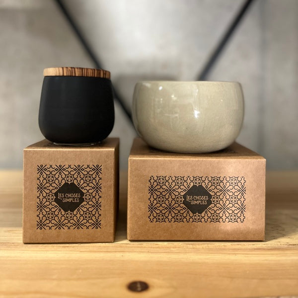 Two ceramic containers, one black and one gray, on wooden boxes with a geometric background.