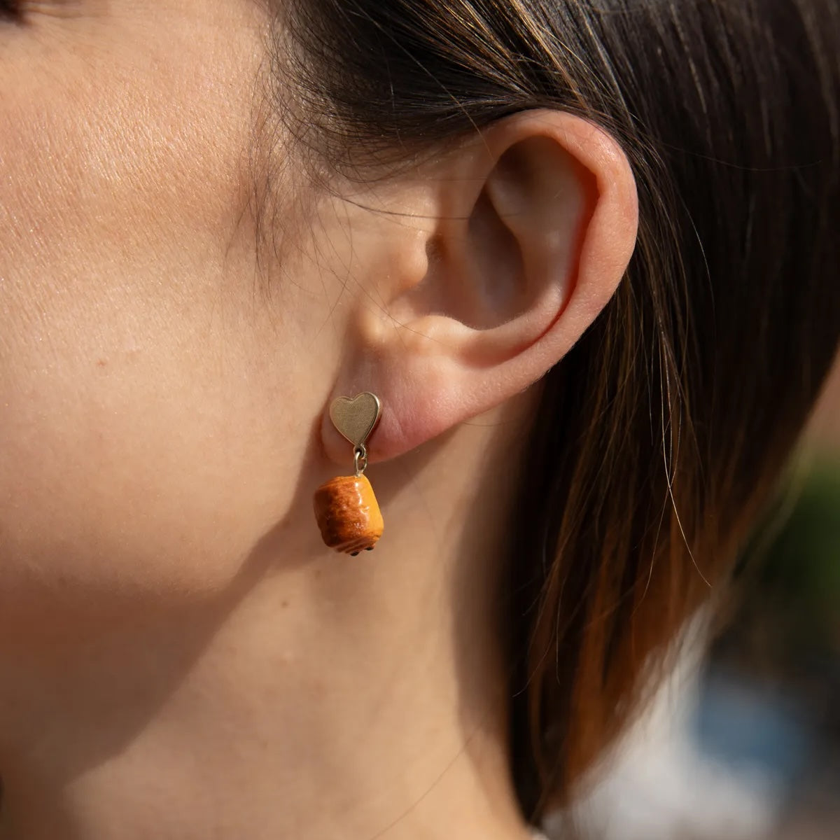 Close-up of a person wearing a chocolatine shaped earring with a small round pendant.