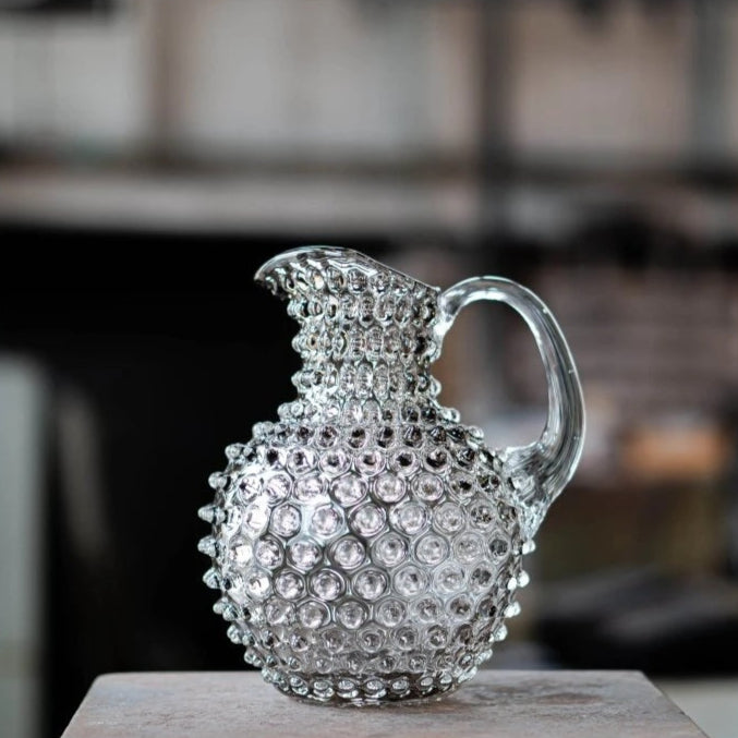 Decorative glass pitcher with crystal embellishments on a wooden surface.