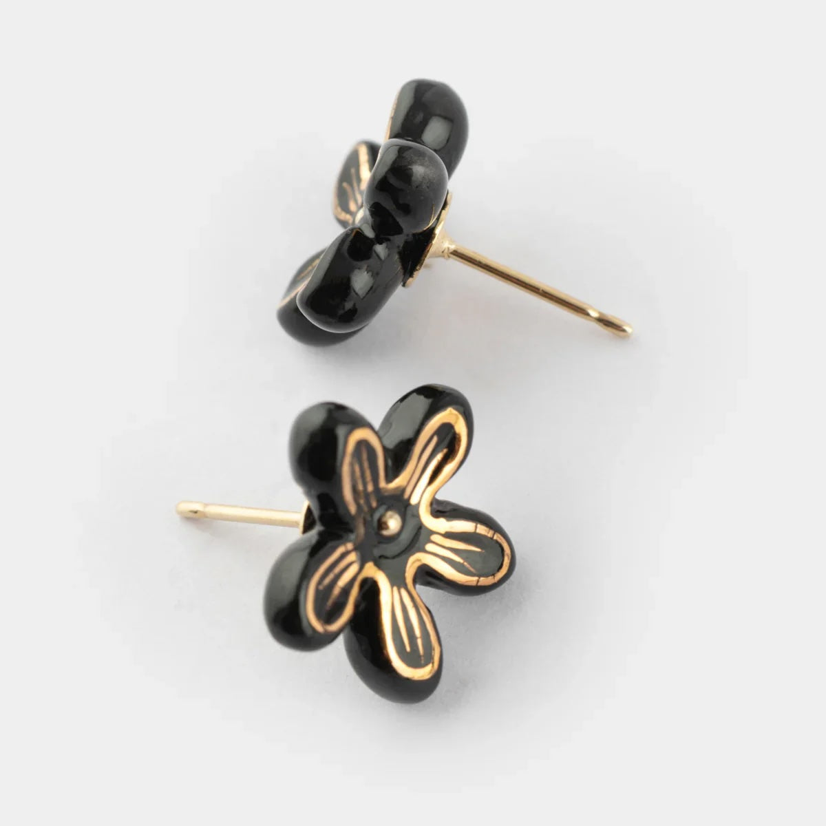A pair of black flower-shaped stud earrings with gold-tone metal outlines and posts, displayed on a clean light gray background.