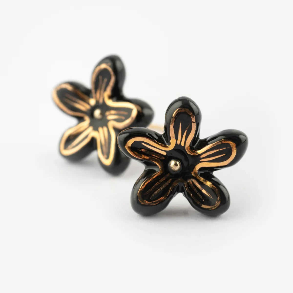 A pair of black flower-shaped stud earrings with gold-tone outlines and center details, shown on a clean white background.
