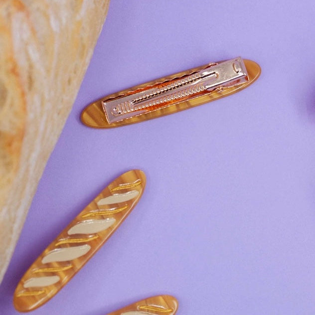 Gold baguette hair clip on a purple surface with a golden baguette on the side