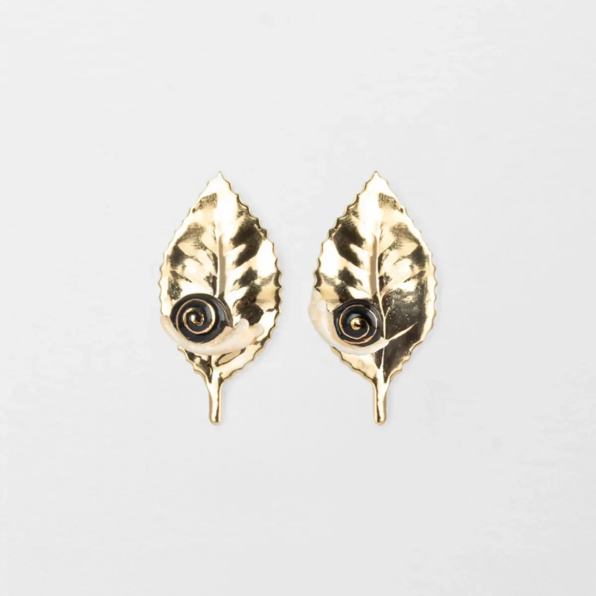 Gold leaf-shaped earrings on a light gray background