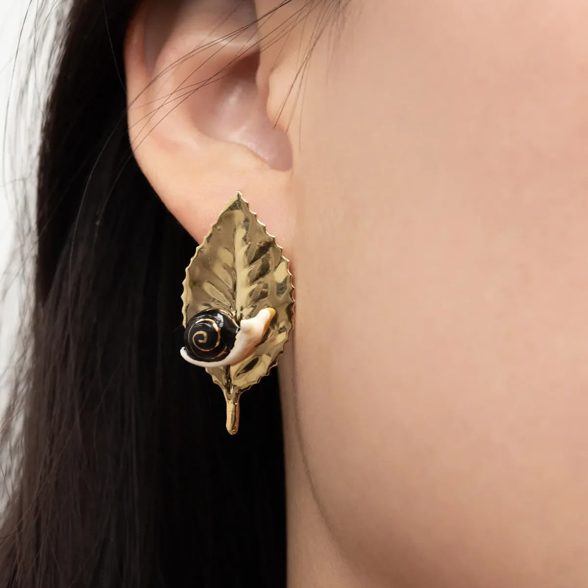 Gold leaf earring worn by a person with dark hair.