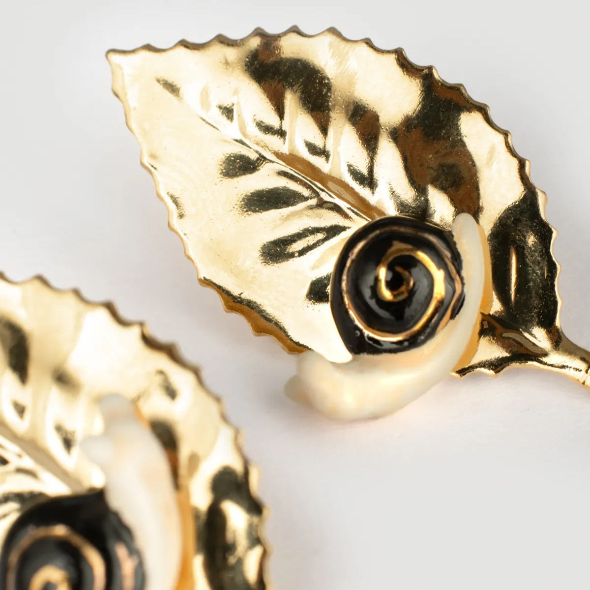 Gold leaf-shaped earrings with a central black rose design on a light gray background