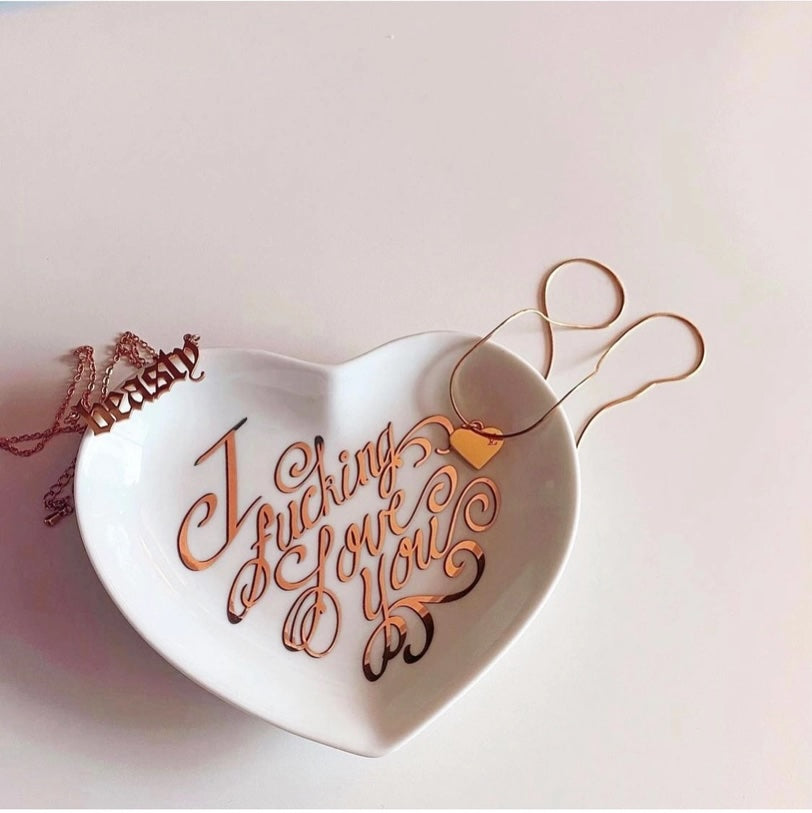 Heart-shaped dish with 'I fucking love you' text on a light pink background