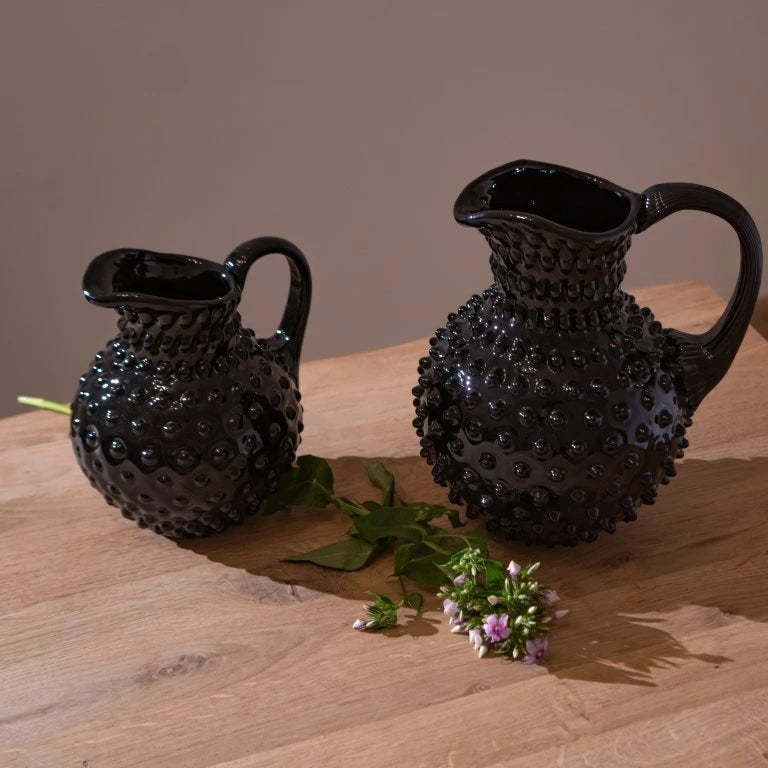 Two black textured glass jugs on a wooden surface with a minimal background