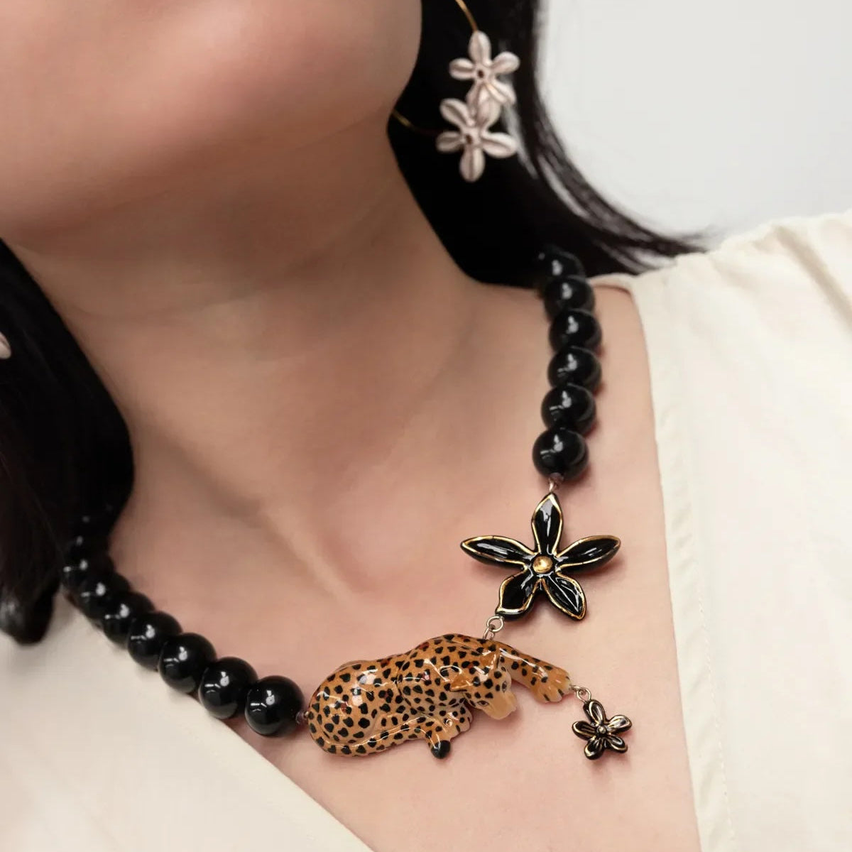 A close-up of a model wearing a black beaded necklace with a leopard-shaped charm and flower charms, paired with matching flower earrings.